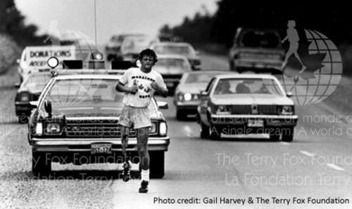 Terry Fox running his Marathon of Hope with vehicles following him during his run.