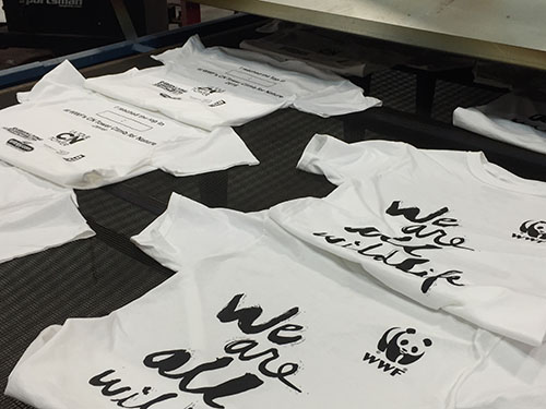 Personalized t-shirts being printed on screen-printing press with custom design for non-profit organization.