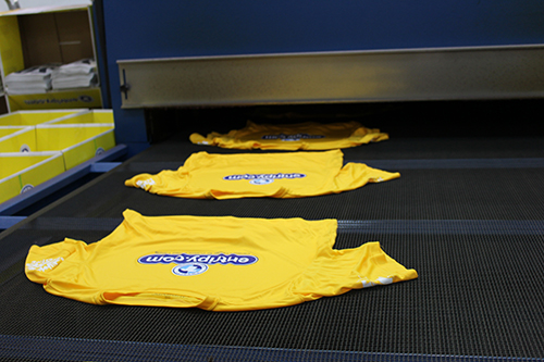 Yellow custom t-shirts coming out from the drying conveyer belt.