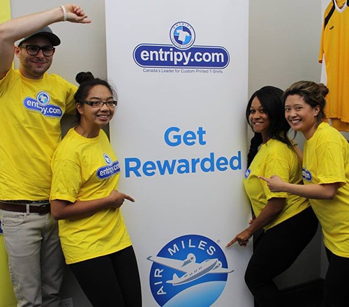 Entripy employees displaying AirMiles and Entripy banner for customer visiting main location to pick up custom apparel orders.